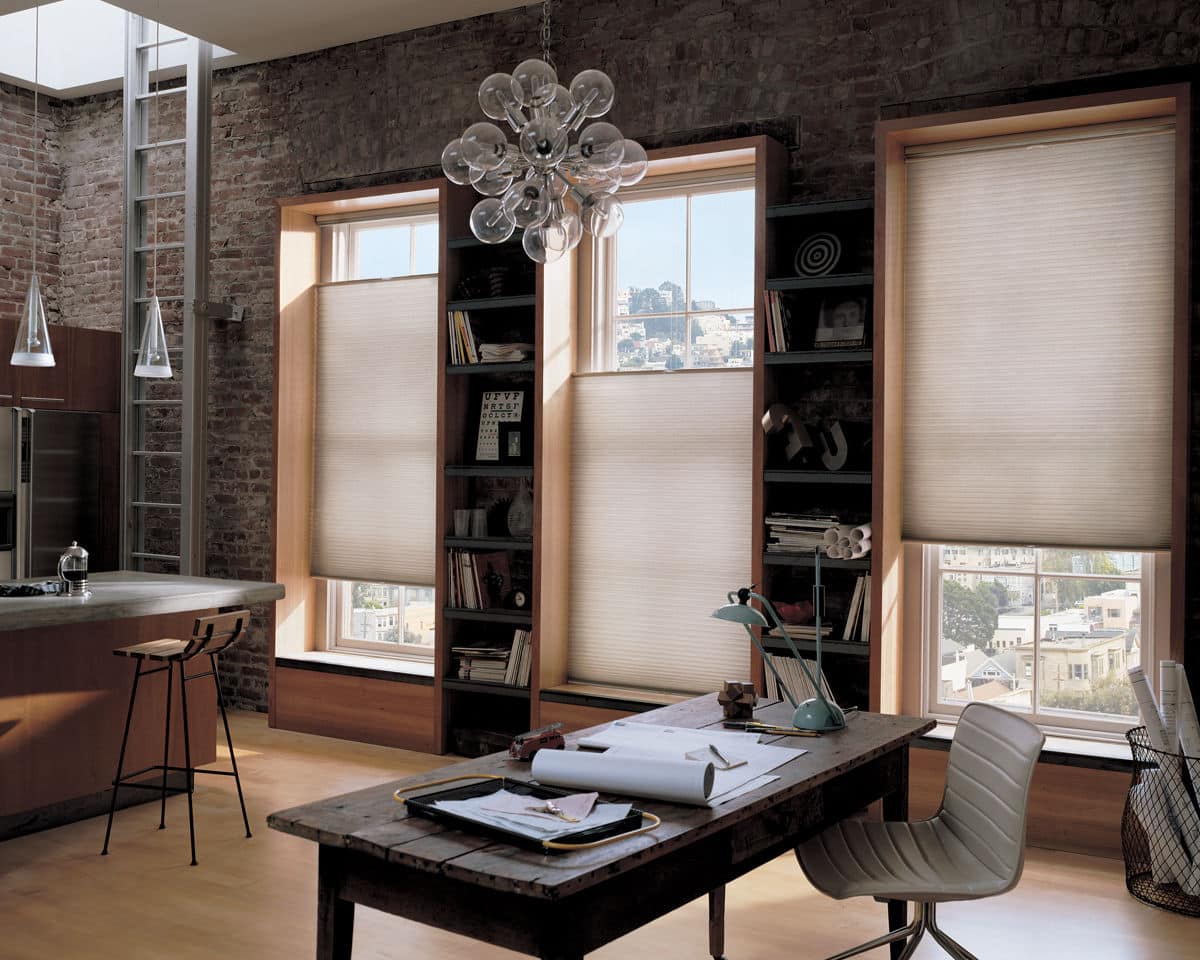 Industrial-style home office and kitchen with exposed brick walls, large windows fitted with honeycomb cellular shades.